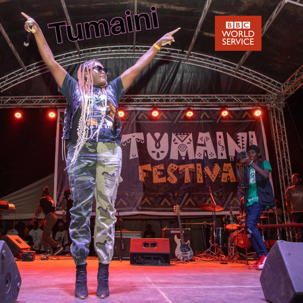 Musician called Beanca with raised arms on stage with Tumaini Festival on banner in the background.